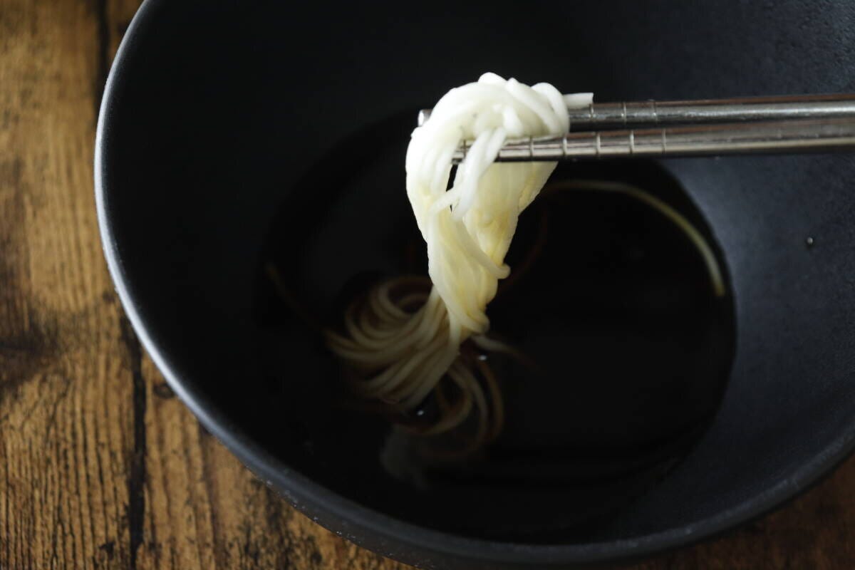 黒い器のめんつゆに、箸でそうめんを浸している手元 黒い器のめんつゆに、箸でそうめんを浸している手元