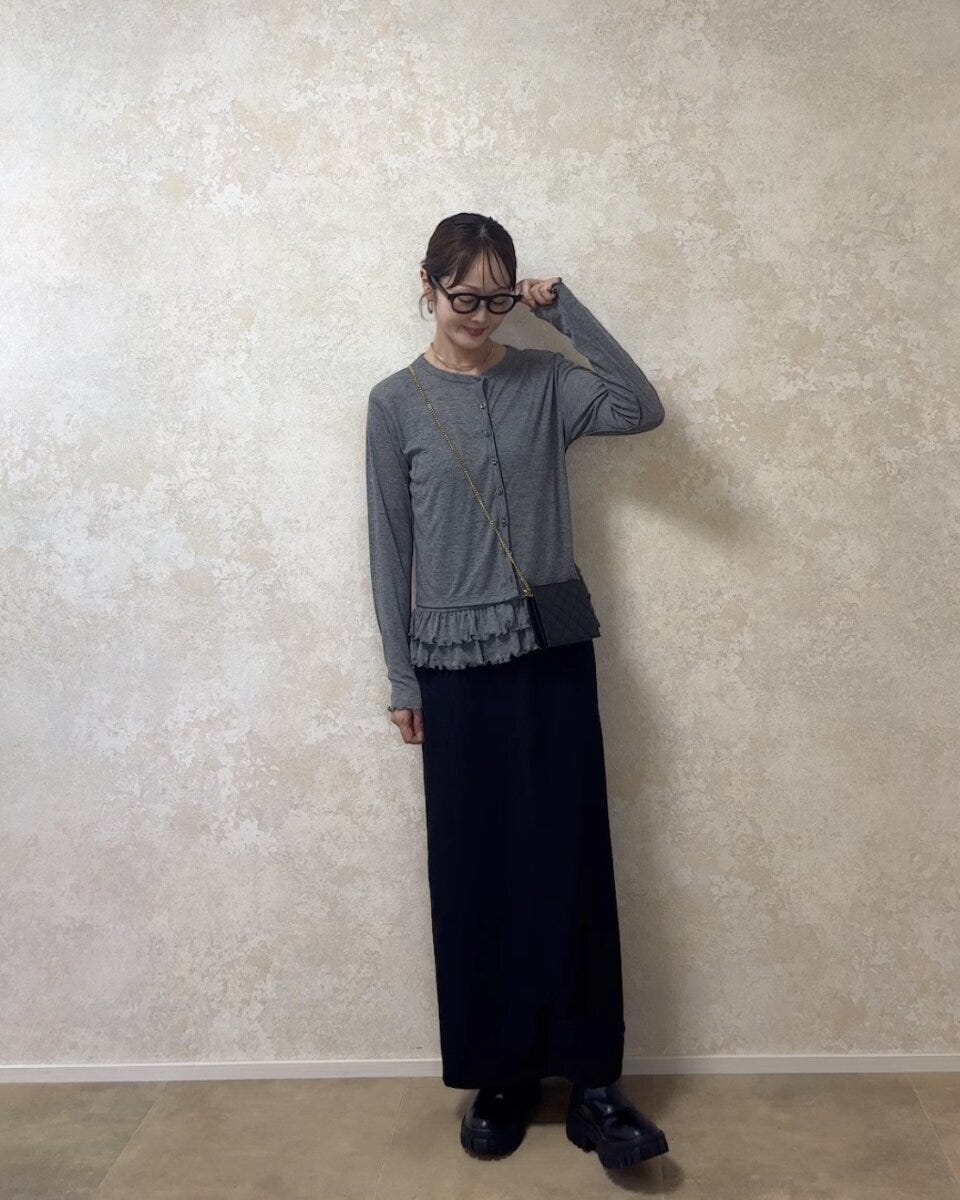 グレーのカーディガンと黒のロングスカートを着用し眼鏡をかけた女性