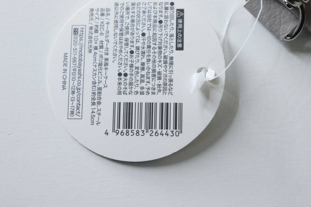 グレーの革風キーケースに付いている商品タグの裏面、JANコードや注意書きが写っている