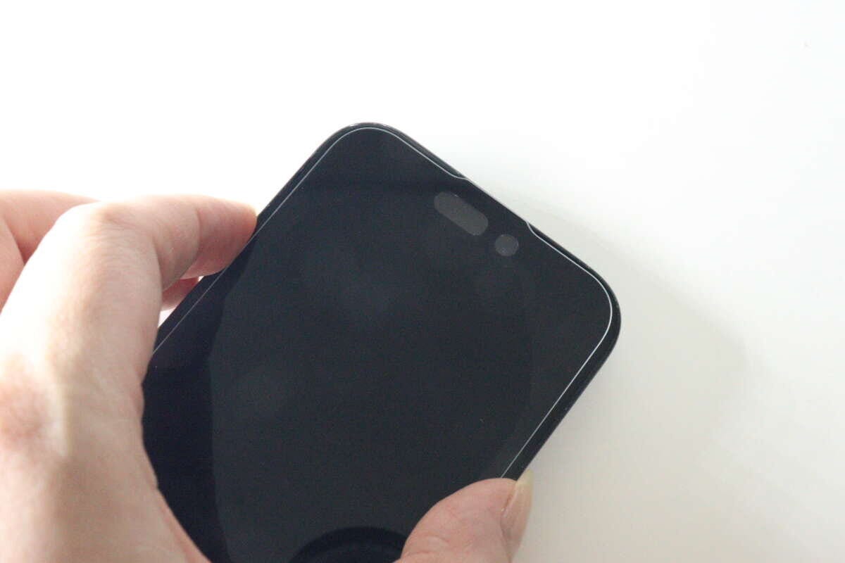 保護ガラスを貼り付けたiPhoneの画面上部を指で押さえている 保護ガラスを貼り付けたiPhoneの画面上部を指で押さえている
