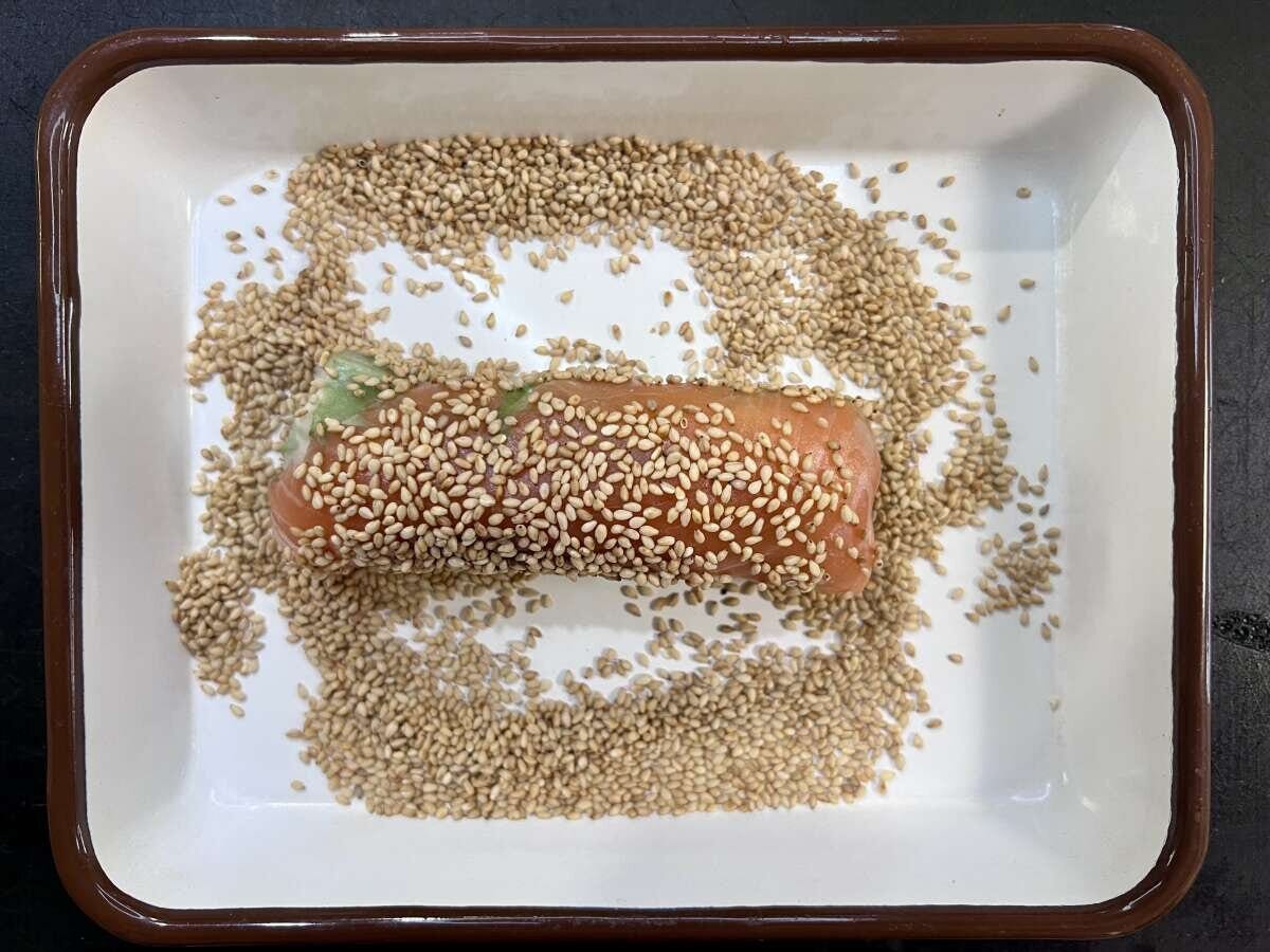 白いりごまを敷き詰めたバットの中で、生春巻きにごまをまぶしている工程の写真