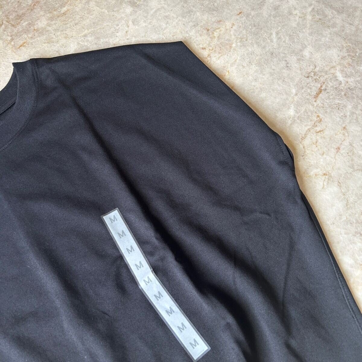 黒いTシャツの肩部分がアップで写っており、タグが複数枚重なっている