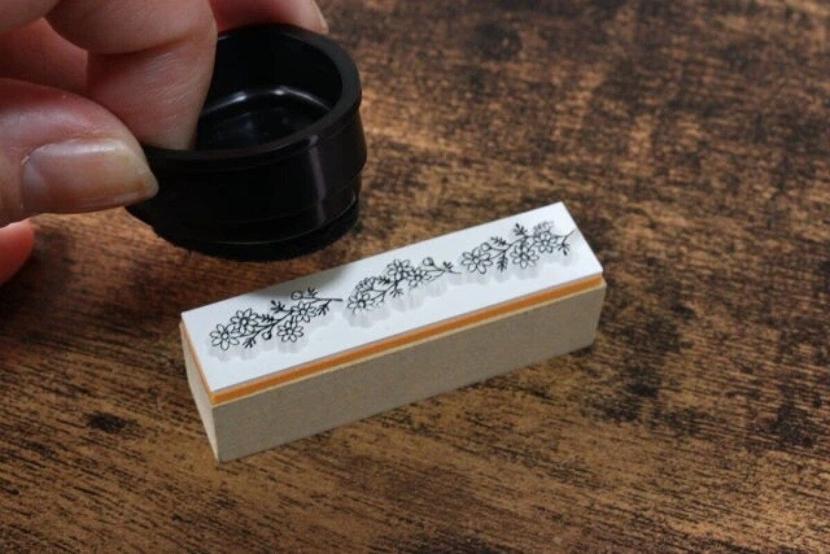 ボタニカル柄のスタンプに黒いインクパッドを押し当ててインクを付けている ボタニカル柄のスタンプに黒いインクパッドを押し当ててインクを付けている