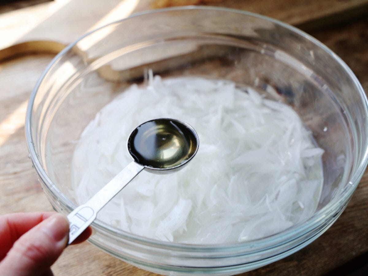 ガラスボウルの酢水に浸けた新玉ねぎスライスに計量スプーンで酢を加える様子 ガラスボウルの酢水に浸けた新玉ねぎスライスに計量スプーンで酢を加える様子