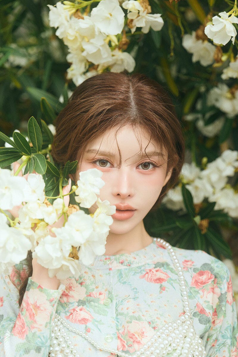 白い花を背景に、花柄の服を着た齊藤早紀さんがカメラを見つめている 白い花を背景に、花柄の服を着た齊藤早紀さんがカメラを見つめている