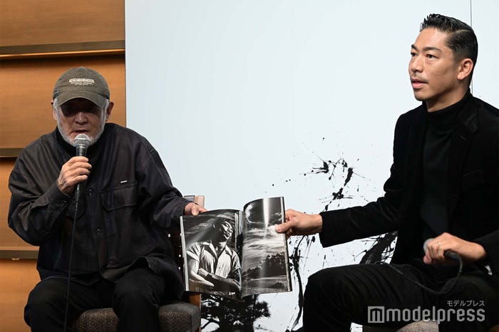 写真集を眺める⻑濱治氏、AKIRA (C)モデルプレス