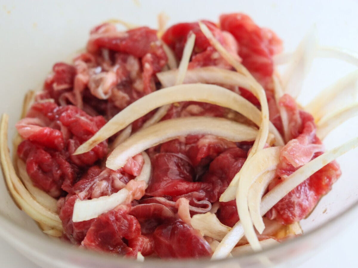 透明なガラスボウルに牛切り落とし肉と薄切り玉ねぎが入っている 透明なガラスボウルに牛切り落とし肉と薄切り玉ねぎが入っている