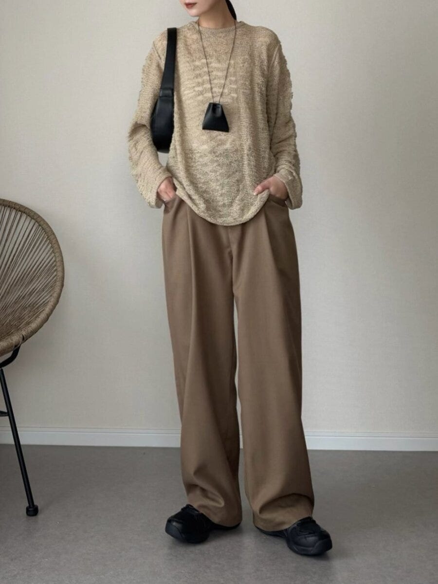 ベージュの透かし編みニットとワイドパンツを着て、黒いバッグを持つ女性