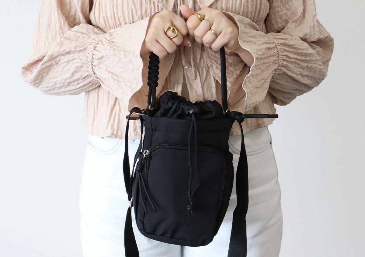 ベージュのブラウスの女性が黒いショルダーバッグをハンドバッグ持ちしている様子