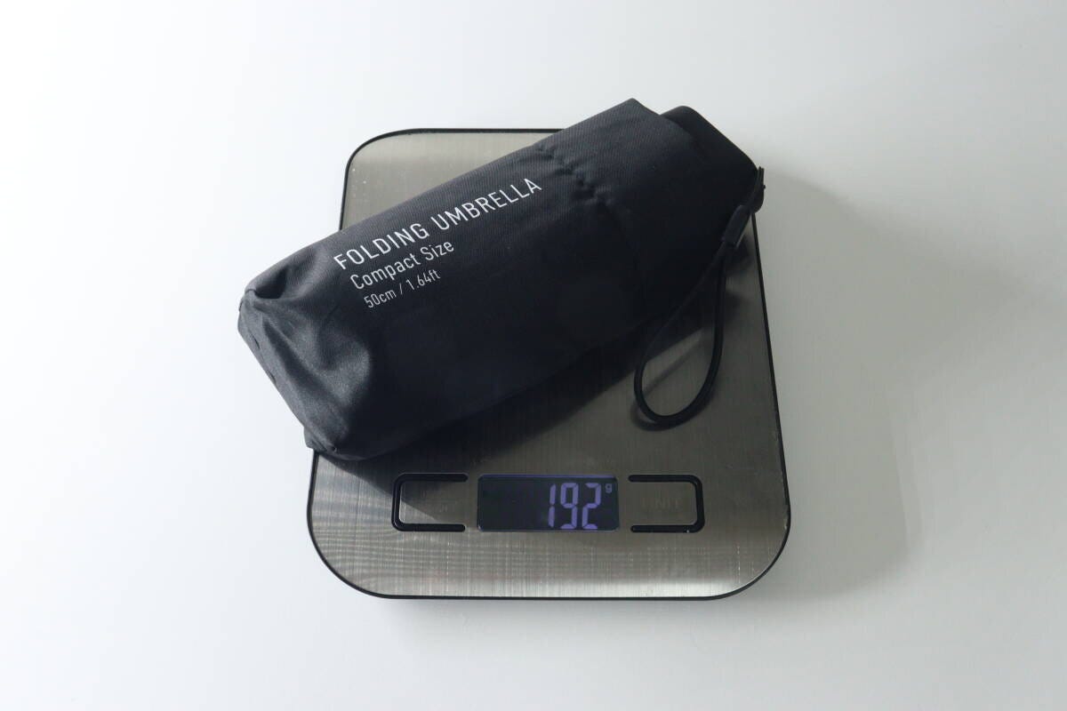 黒い折りたたみ傘をキッチンスケールに乗せ、192gと表示された重さを測っている