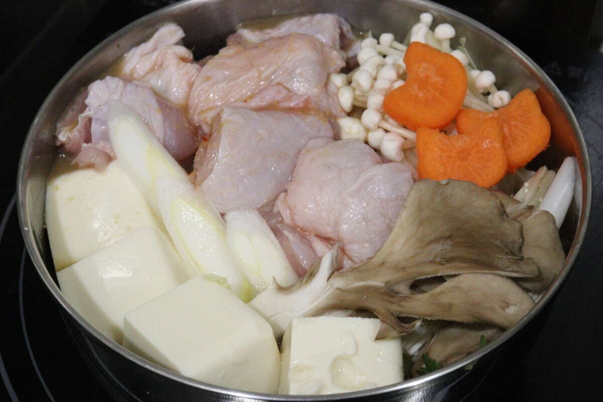 鍋に鶏肉や豆腐、きのこやにんじんなどの具材を並べた状態