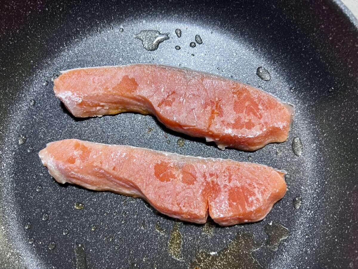 熱したフライパンにサラダ油をひき、2切れの鮭が焼かれている