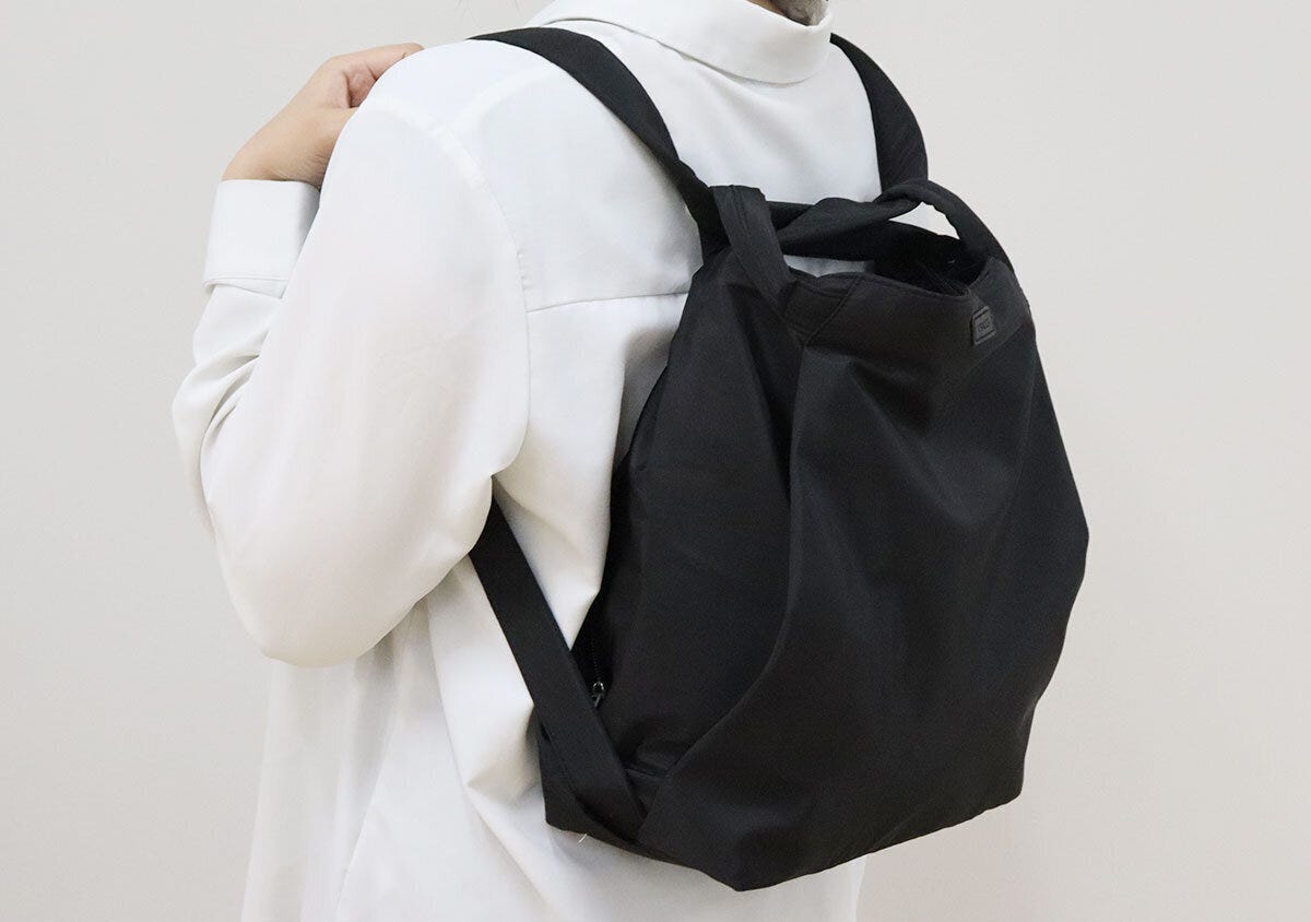 白シャツの女性が黒いバッグをリュックとして背負う