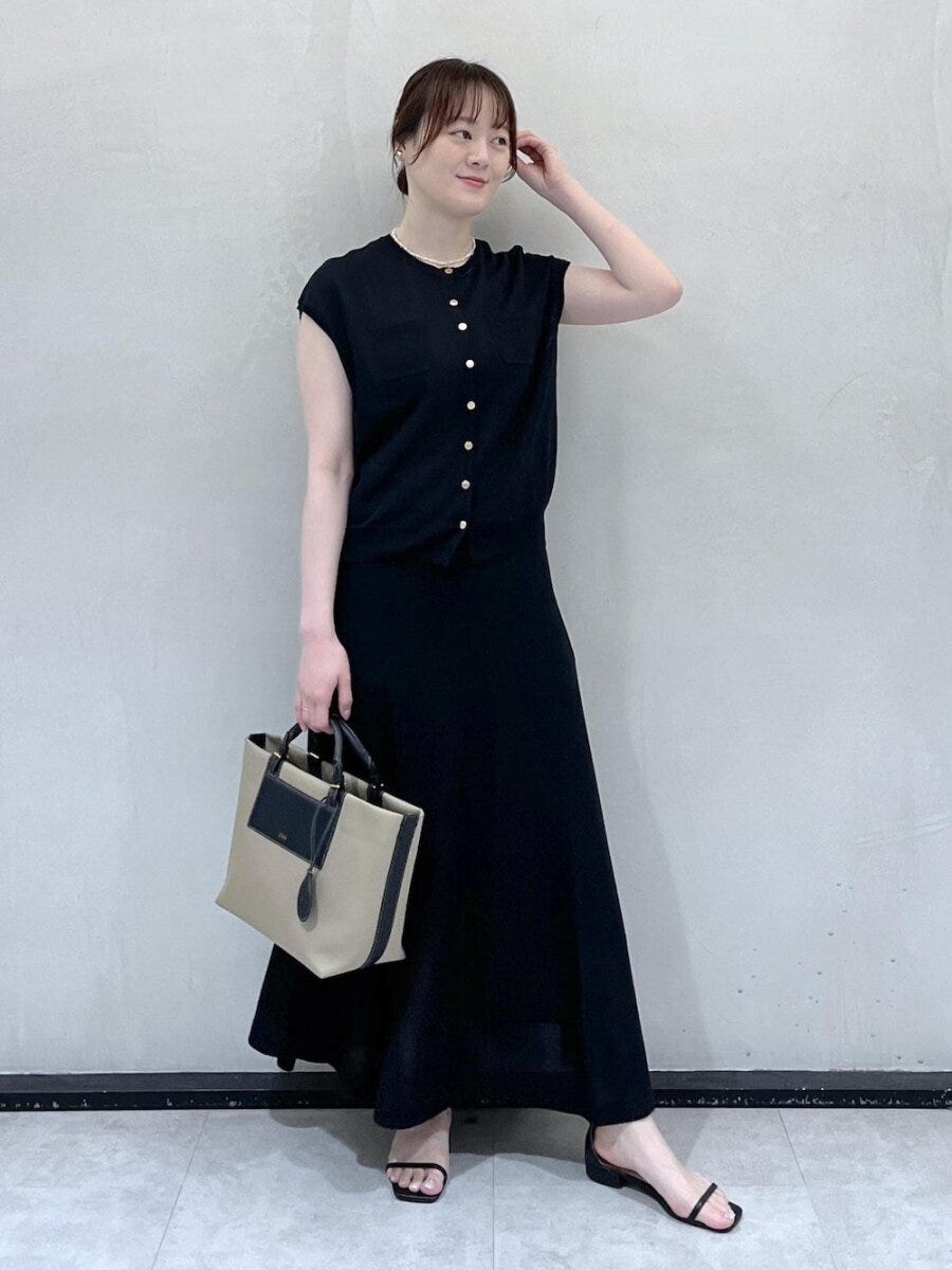 黒いニットとロングスカートを着てベージュのバッグを持つ女性