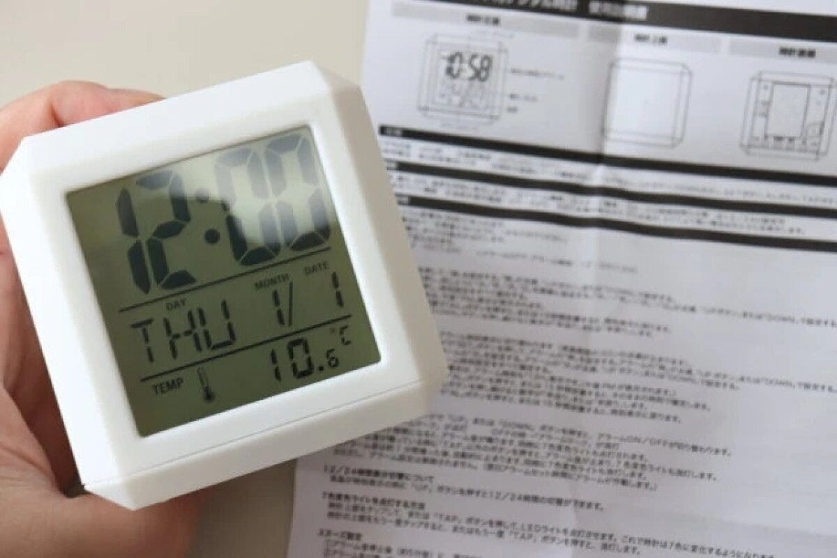 白い「7色変色ライト付デジタル時計」を手に持ち、説明書を広げた状態 白い「7色変色ライト付デジタル時計」を手に持ち、説明書を広げた状態