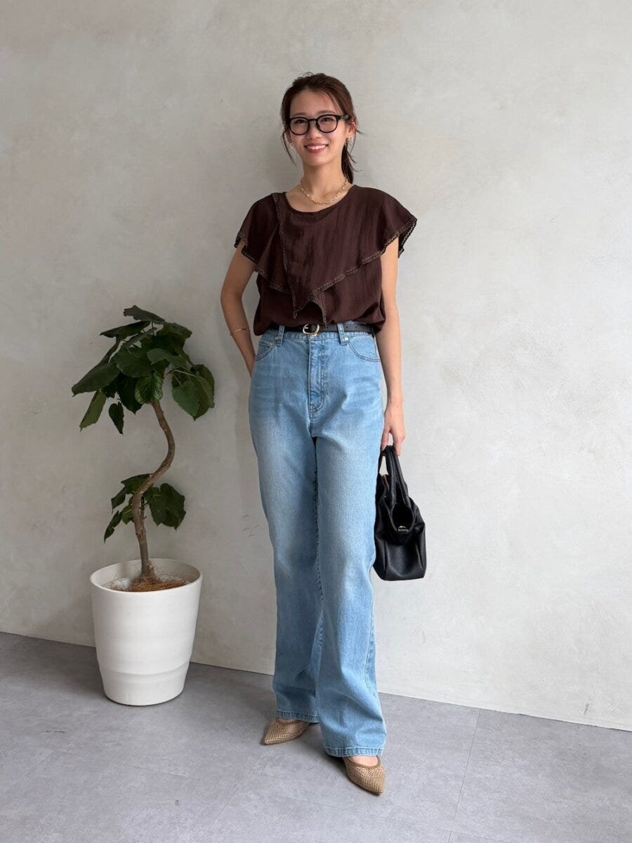 ブラウンブラウスとデニムを着用し笑顔で立つ女性