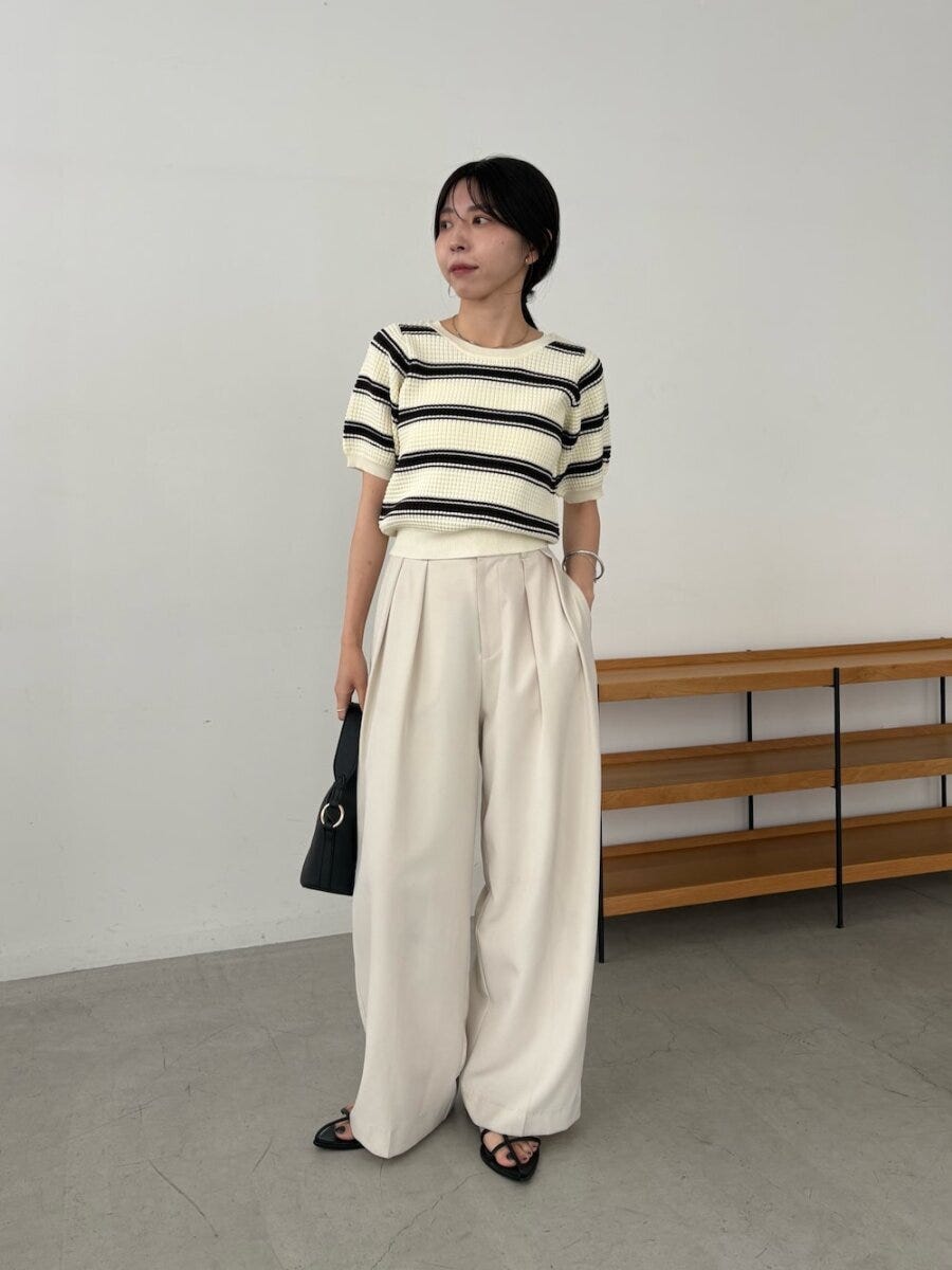 白黒ボーダーニットと白ワイドパンツの女性が黒バッグを持ち横を向く全身