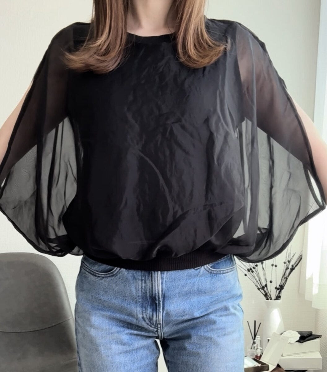 黒いシアーケープブラウスとデニムを着用し両腕を広げた女性の正面アップ