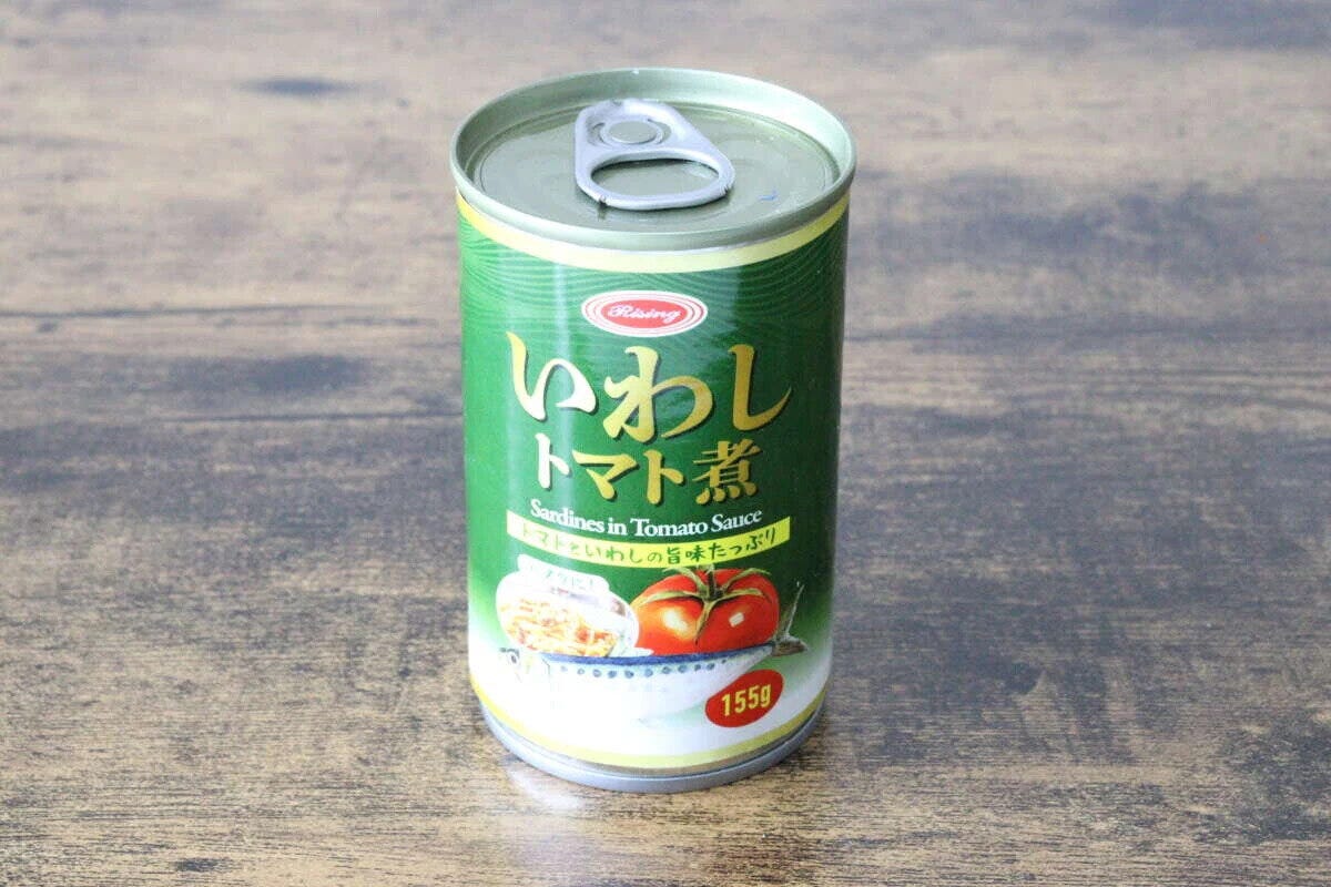 緑色の「いわしトマト煮」缶詰が木目のテーブルに置かれている 緑色の「いわしトマト煮」缶詰が木目のテーブルに置かれている