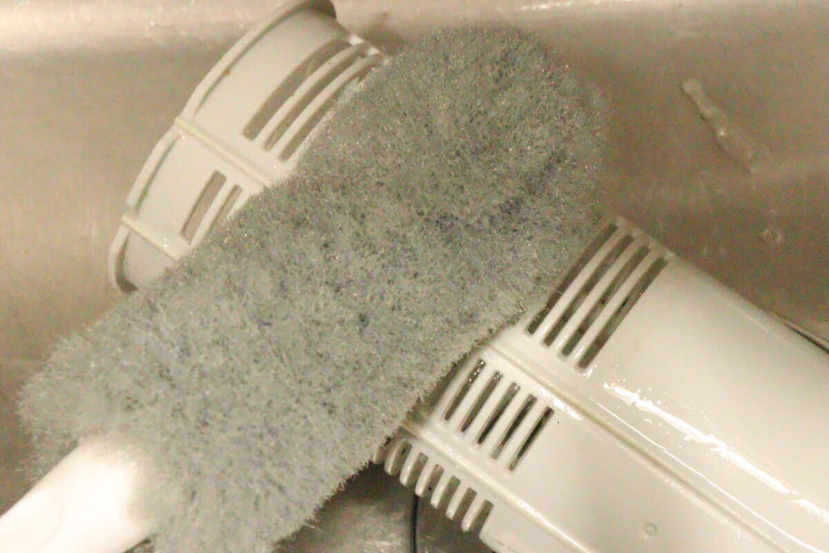 排水バスケットクリーナーでキッチンの排水バスケットの側面をこすり洗いしている様子