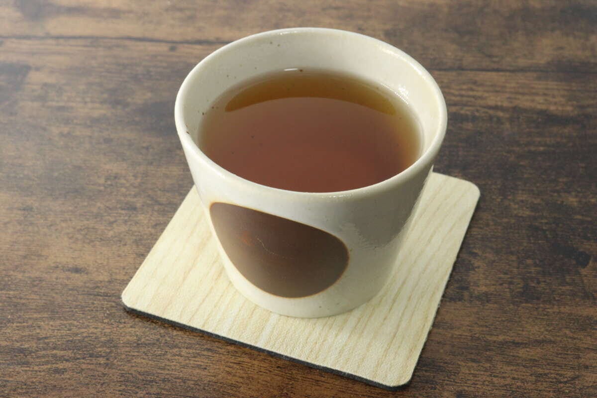 茶碗に入った琥珀色の温かいごぼう茶がコースターの上に置かれている 茶碗に入った琥珀色の温かいごぼう茶がコースターの上に置かれている