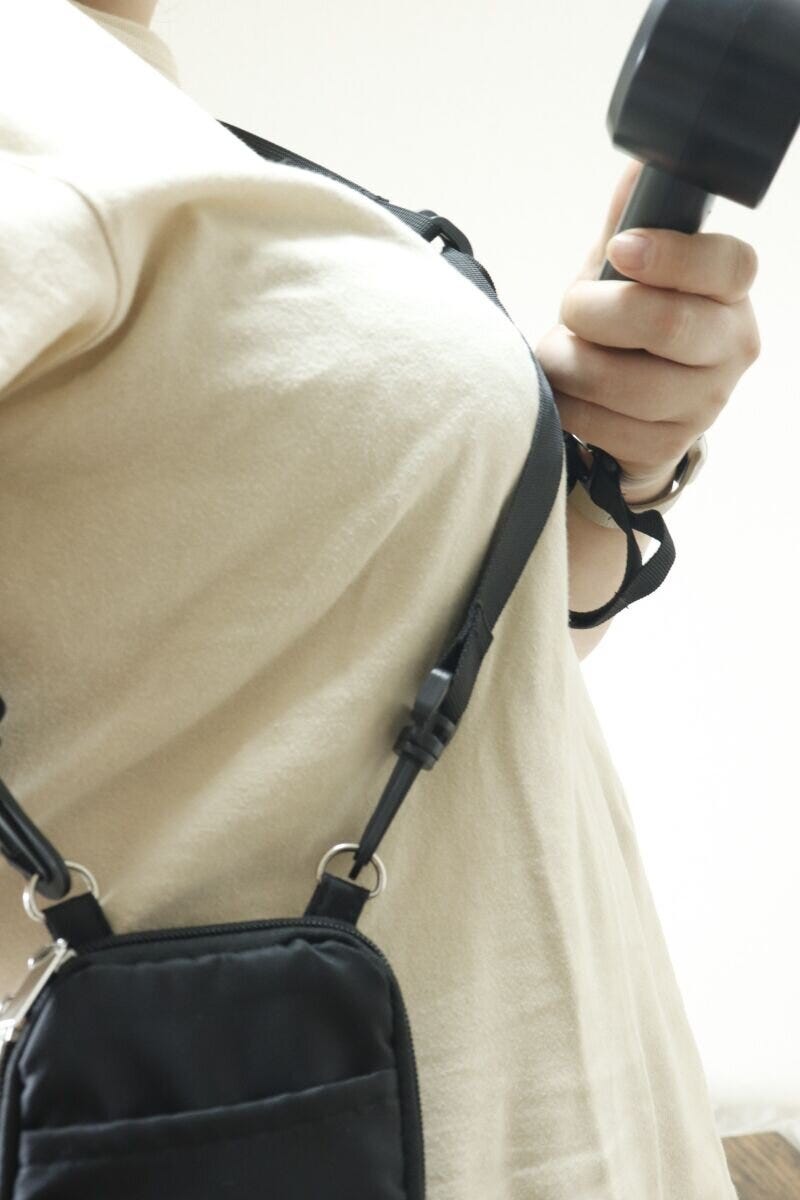 ベージュの服を着た女性がストラップを肩にかけ、ハンディファンを手に持っている