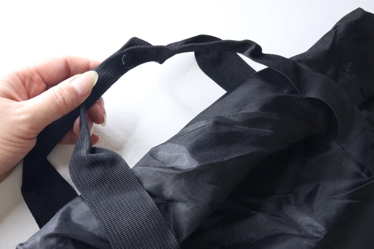 女性の手が、黒いトート型バックパックの持ち手同士を留めるホックを操作している。