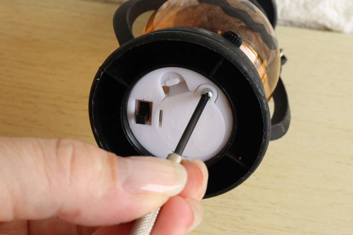 女性がLEDランタンの底面の電池蓋をドライバーで開けている 女性がLEDランタンの底面の電池蓋をドライバーで開けている