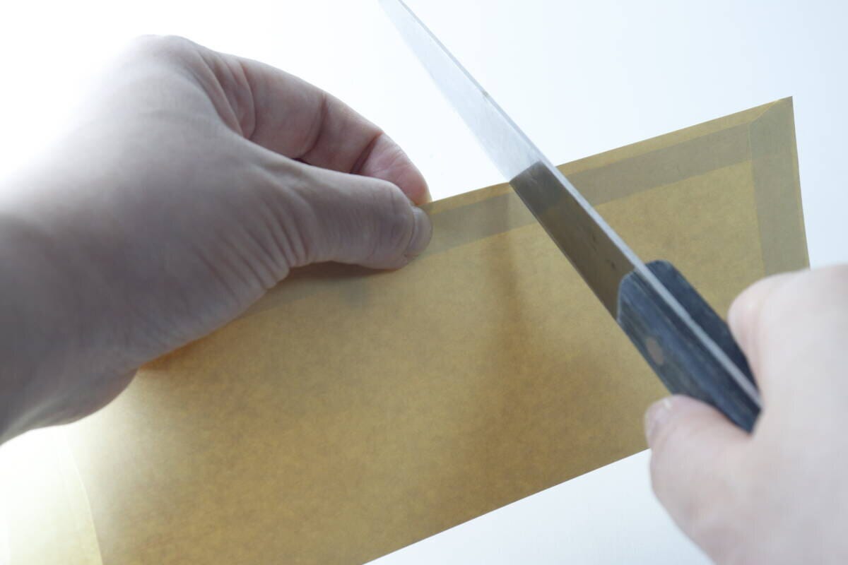切れ味の悪い包丁で封筒を切ろうとしている手元