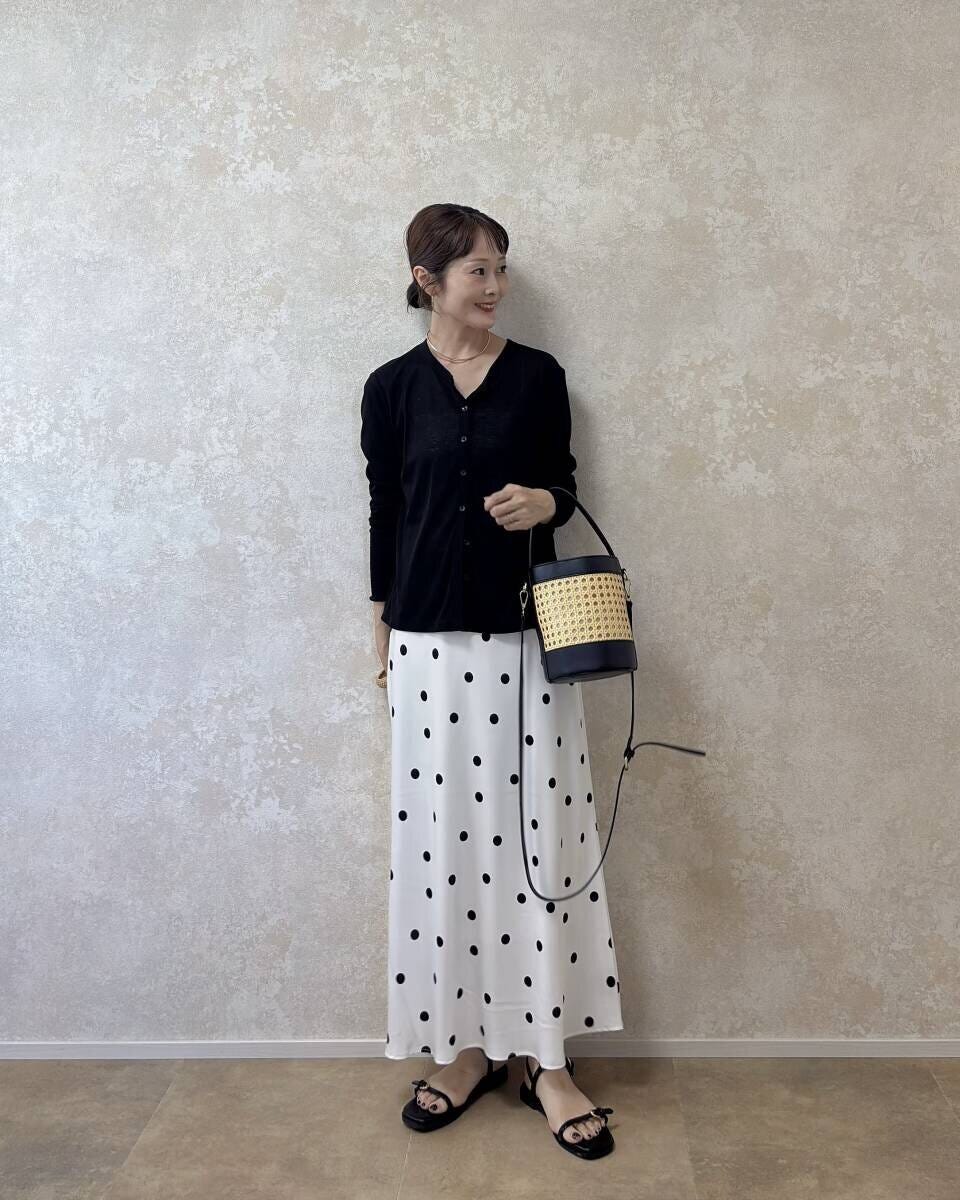 白のドット柄スカートと黒いカーディガンを着た女性が斜めを向いて立っている