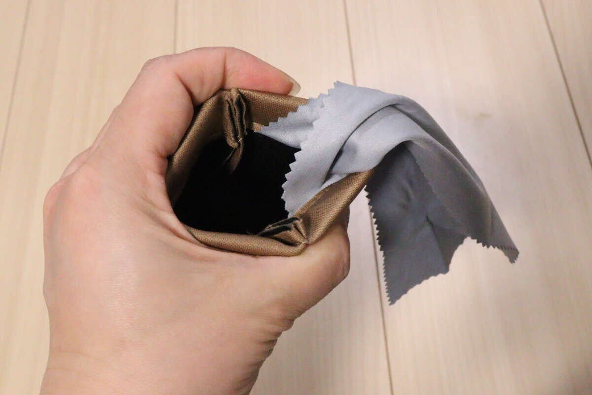 ばね口を開いた茶色のケースからグレーのメガネ拭きが覗く