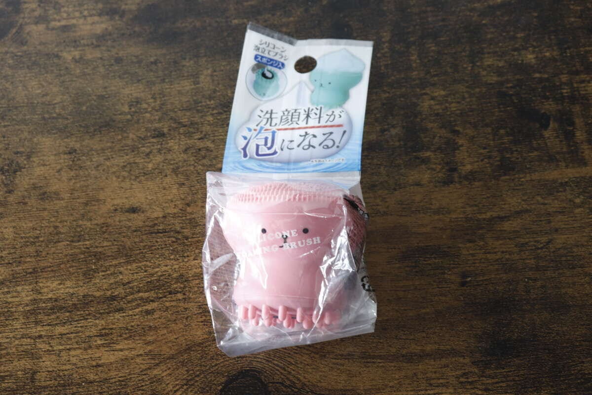 パッケージに入ったピンク色の洗顔ブラシが木目のテーブルに置かれている パッケージに入ったピンク色の洗顔ブラシが木目のテーブルに置かれている