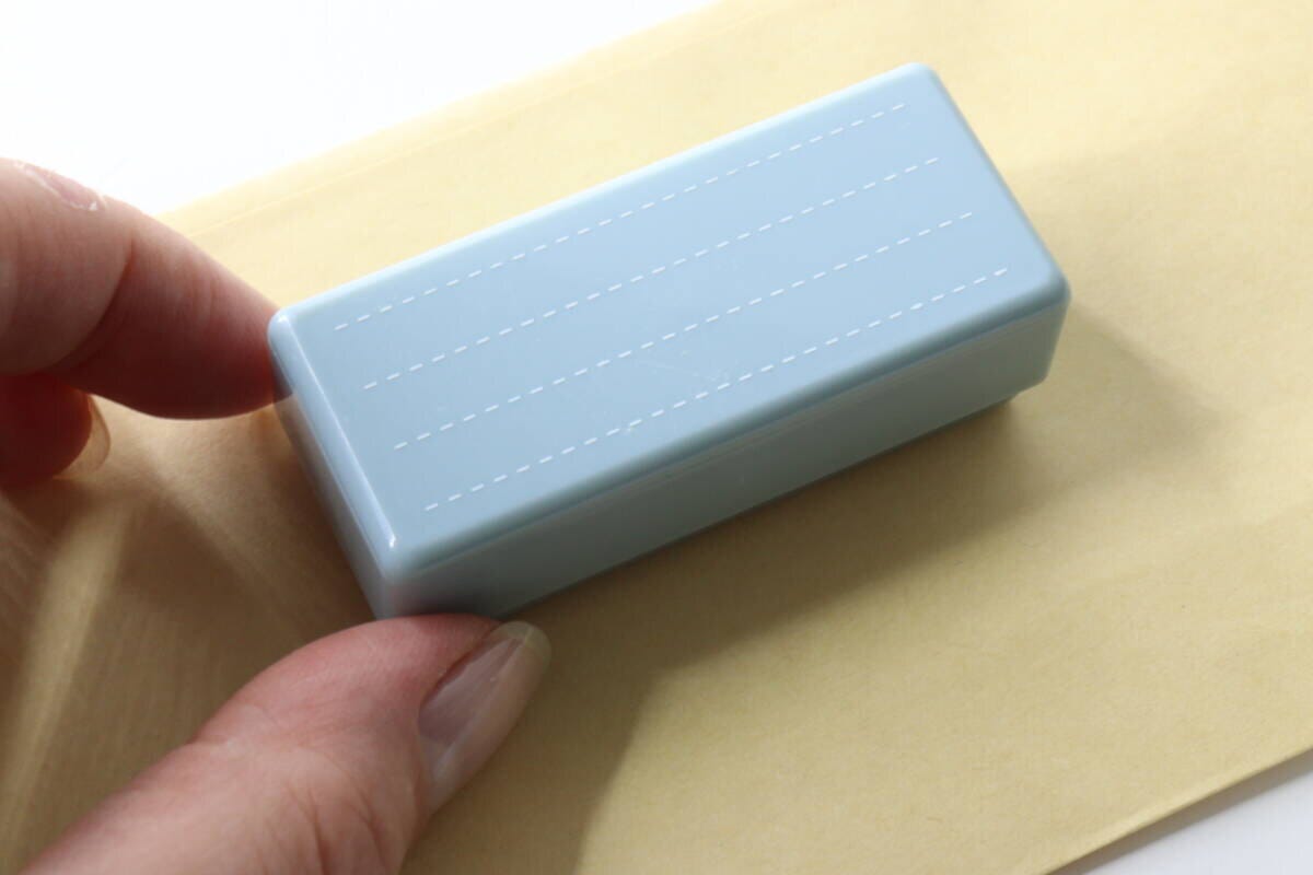 女性がセリアの罫線練習スタンプを薄茶色の紙に押そうとしている