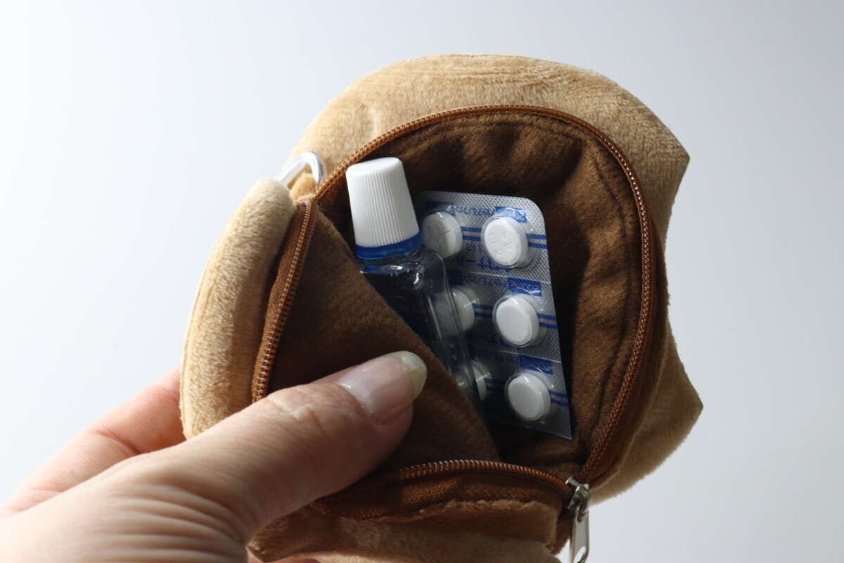 女性の指がクッキー型ポーチのファスナーを開け、目薬と錠剤の薬が入っている様子 女性の指がクッキー型ポーチのファスナーを開け、目薬と錠剤の薬が入っている様子