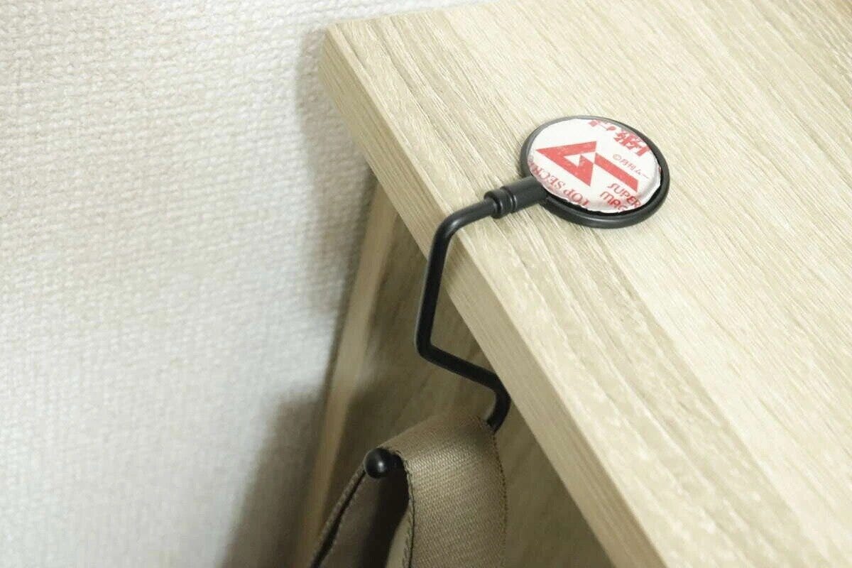 黒いバッグフックが木目調のテーブルの縁に設置され、下にバッグが掛けられている 黒いバッグフックが木目調のテーブルの縁に設置され、下にバッグが掛けられている