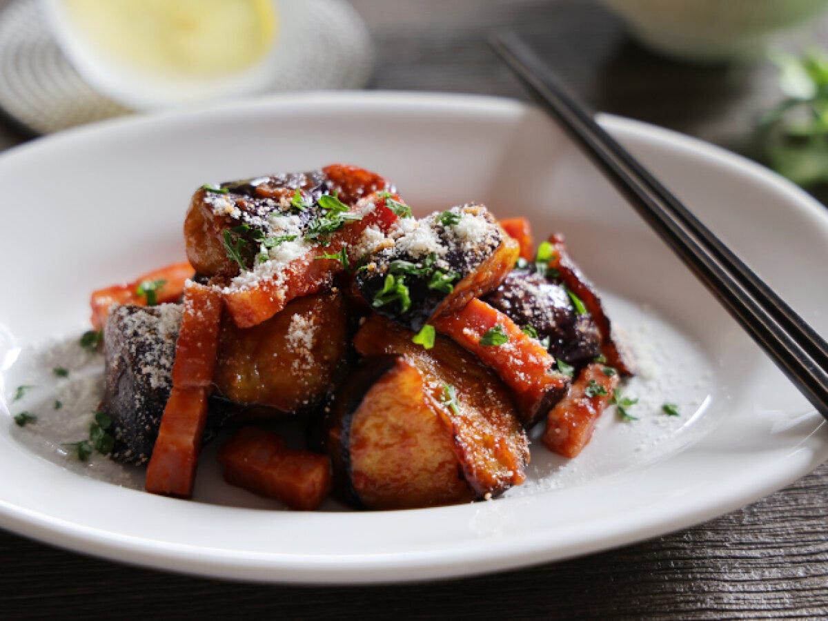 白い皿に盛られたなすとベーコンの和風ケチャップ炒め。粉チーズと刻みパセリが散らされている。 白い皿に盛られたなすとベーコンの和風ケチャップ炒め。粉チーズと刻みパセリが散らされている。