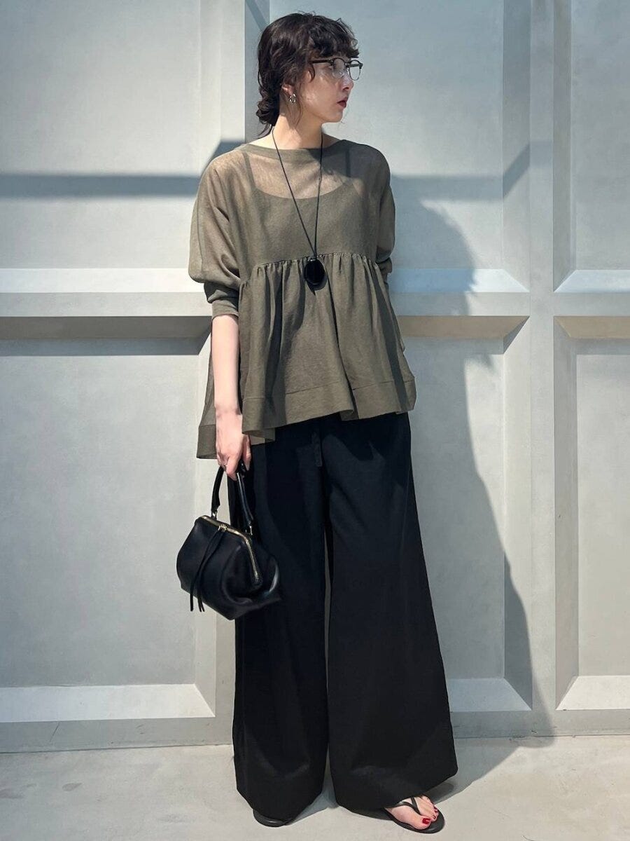 カーキのペプラムシアートップスと黒ワイドパンツ、黒のハンドバッグを持つ女性 カーキのペプラムシアートップスと黒ワイドパンツ、黒のハンドバッグを持つ女性