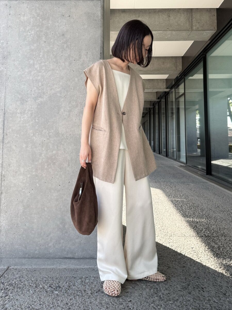 ベージュのジレと白いワイドパンツを着用し、茶色いバッグを持つ女性 ベージュのジレと白いワイドパンツを着用し、茶色いバッグを持つ女性