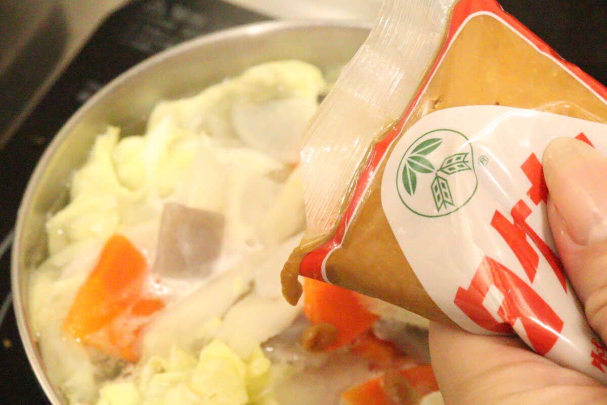 鍋の野菜にタケヤ特醸みそパックから味噌を絞り入れる手元