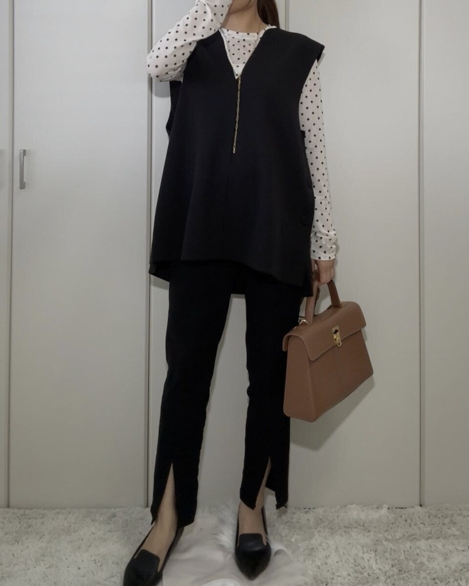 白いドット柄のシアーTシャツに黒いベストとパンツ、茶色のハンドバッグを合わせた全身コーデの女性