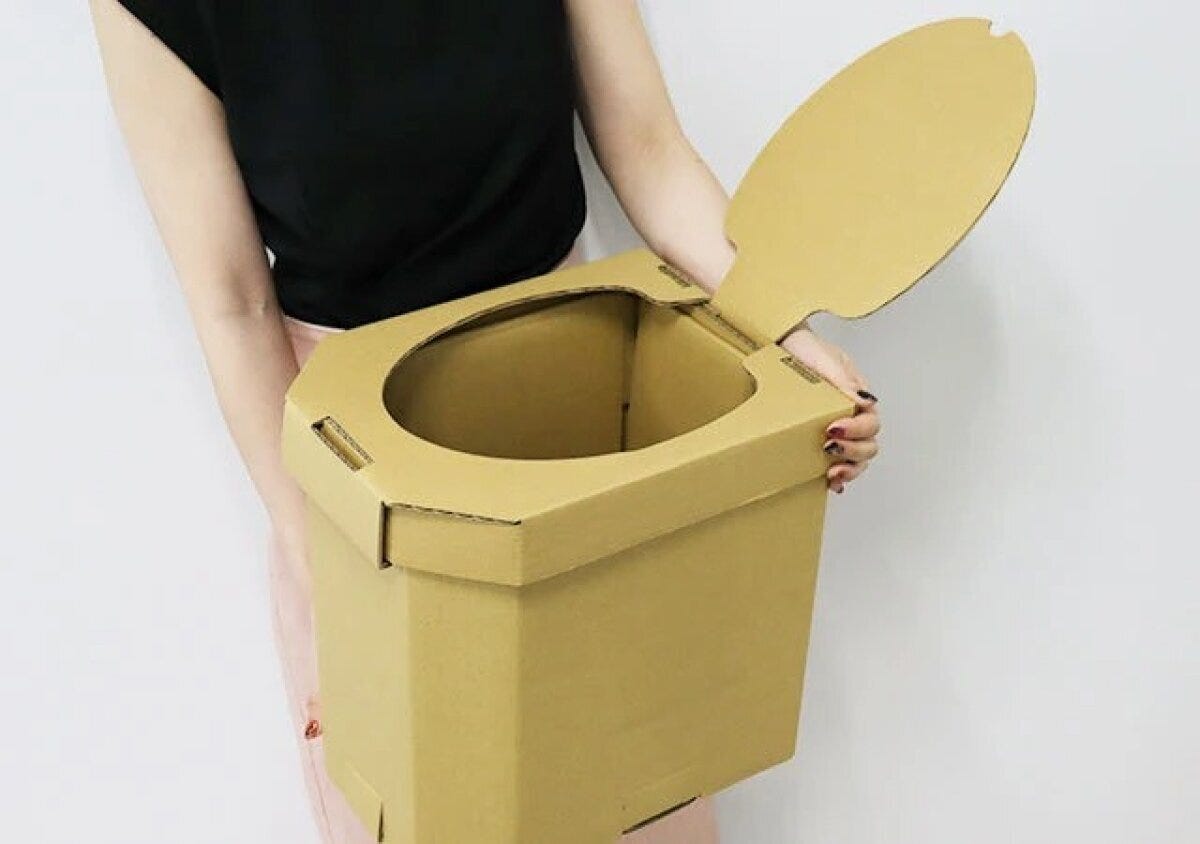 女性が組み立てられた茶色い段ボール製簡易トイレを両手で持っている