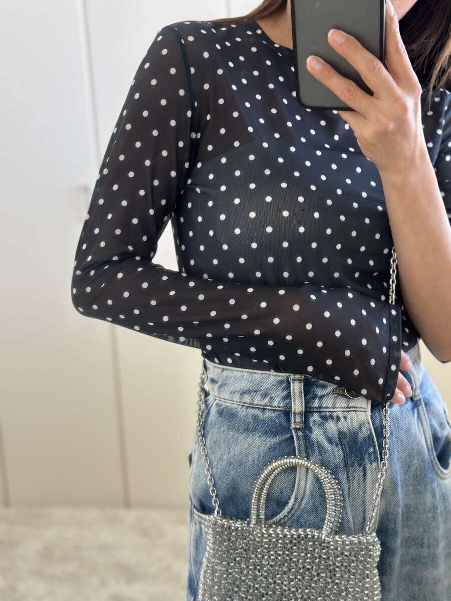 黒いドット柄のシアーTシャツとダメージデニムを着用し、シルバーのミニバッグを持つ女性のウエストアップ