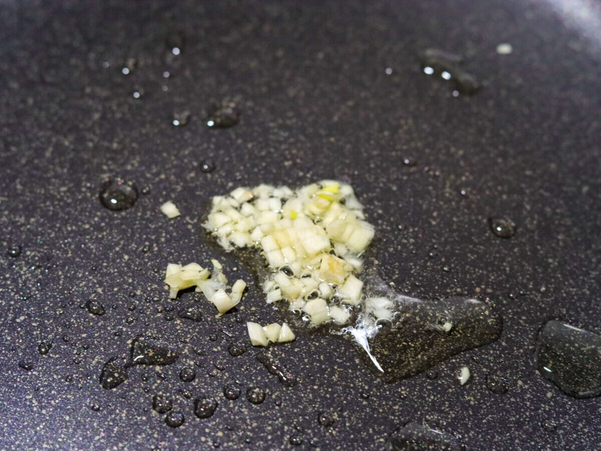 フライパンにオリーブオイルとみじん切りにんにくを入れ弱火で加熱している工程のクローズアップ写真