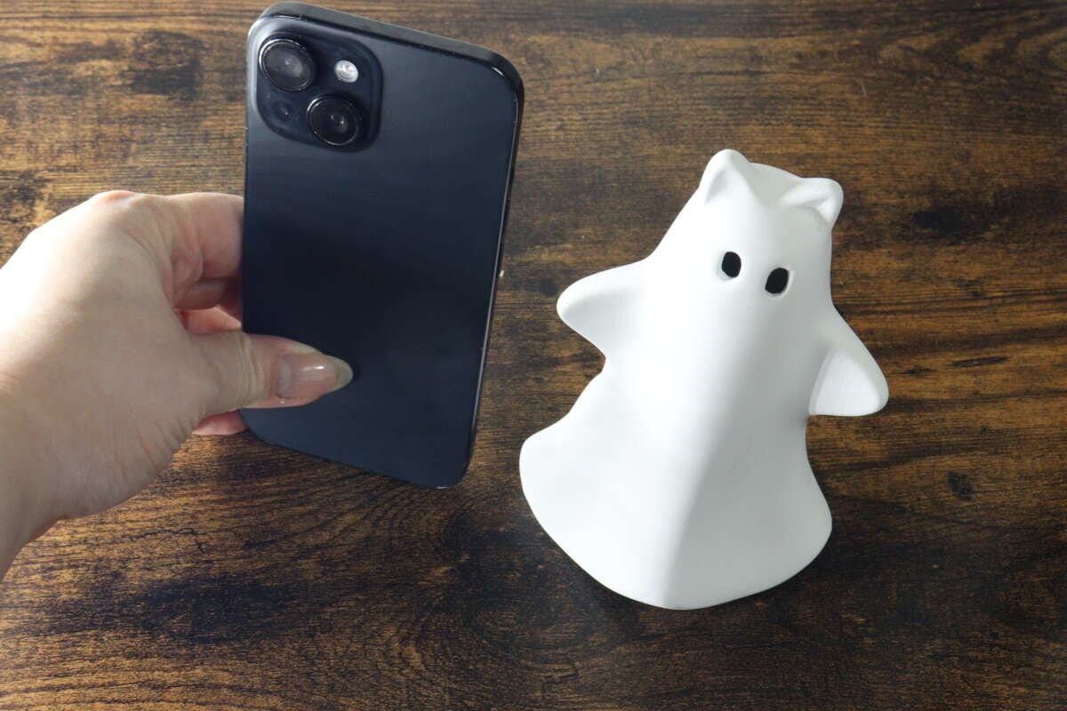 白いゴーストオブジェの横にスマートフォンを置いてサイズを比較している 白いゴーストオブジェの横にスマートフォンを置いてサイズを比較している