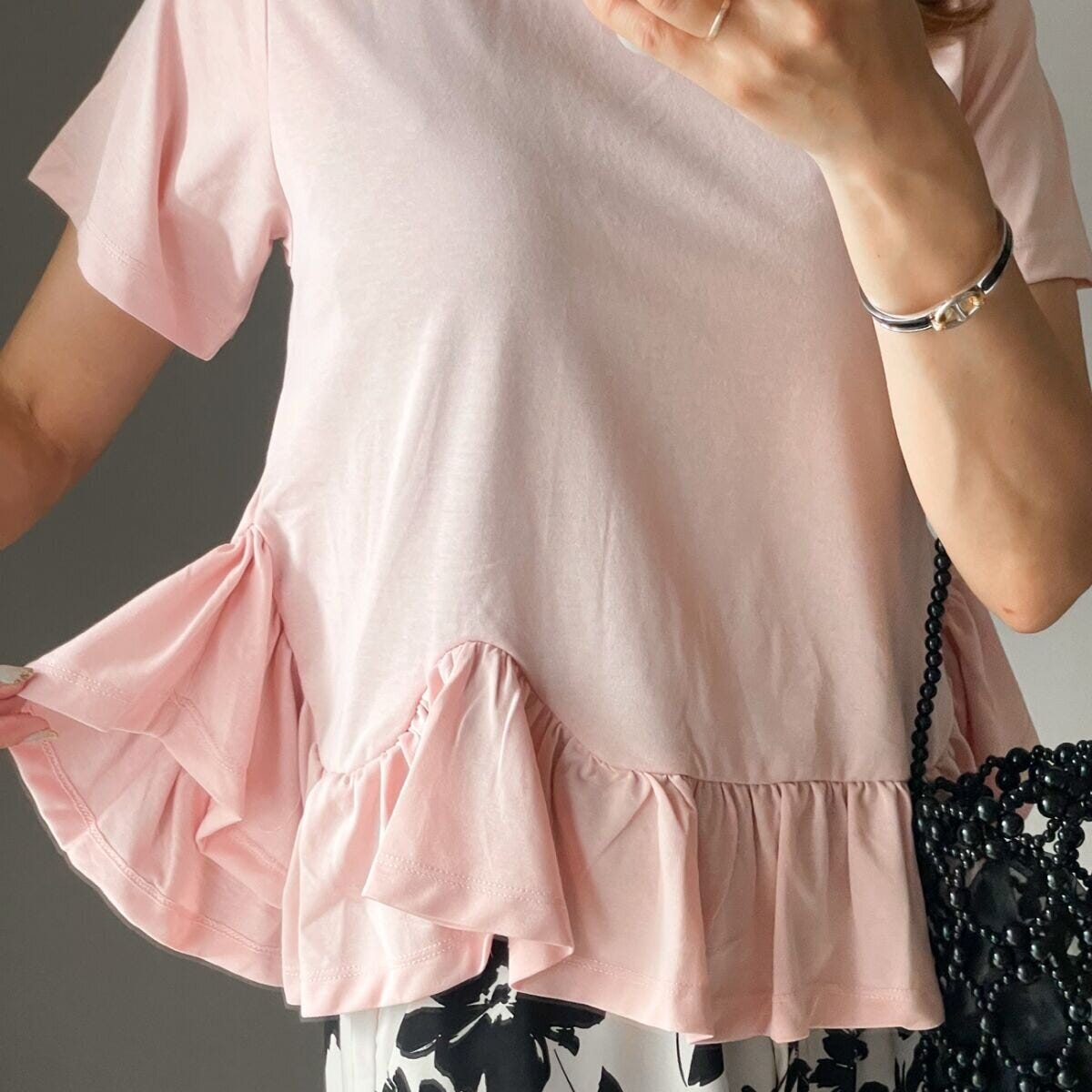 ピンクのペプラムトップスと花柄スカートの女性。フリルをつまんで見せている。