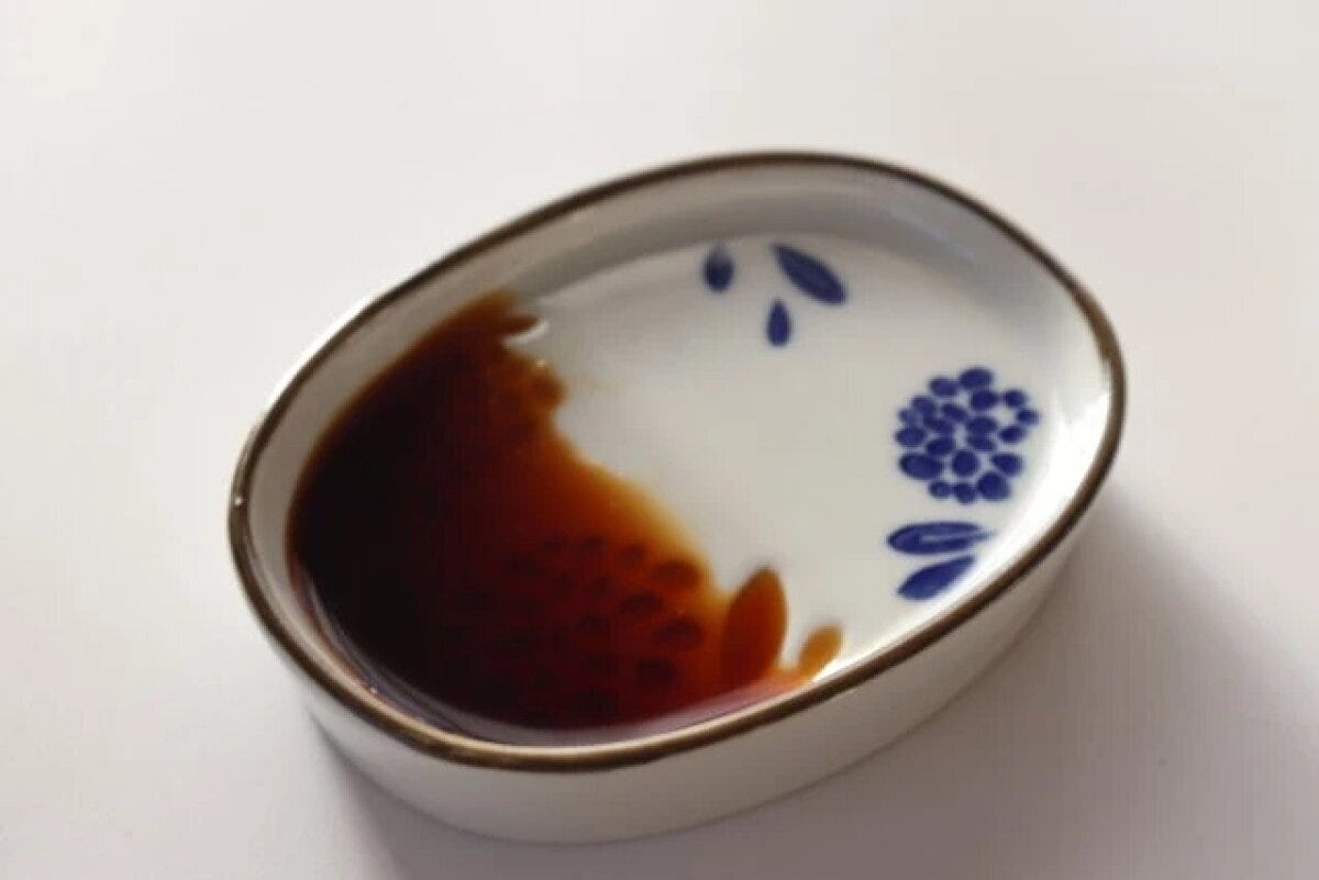 白いななめ醤油皿に醤油が注がれ、傾斜に溜まっている 白いななめ醤油皿に醤油が注がれ、傾斜に溜まっている