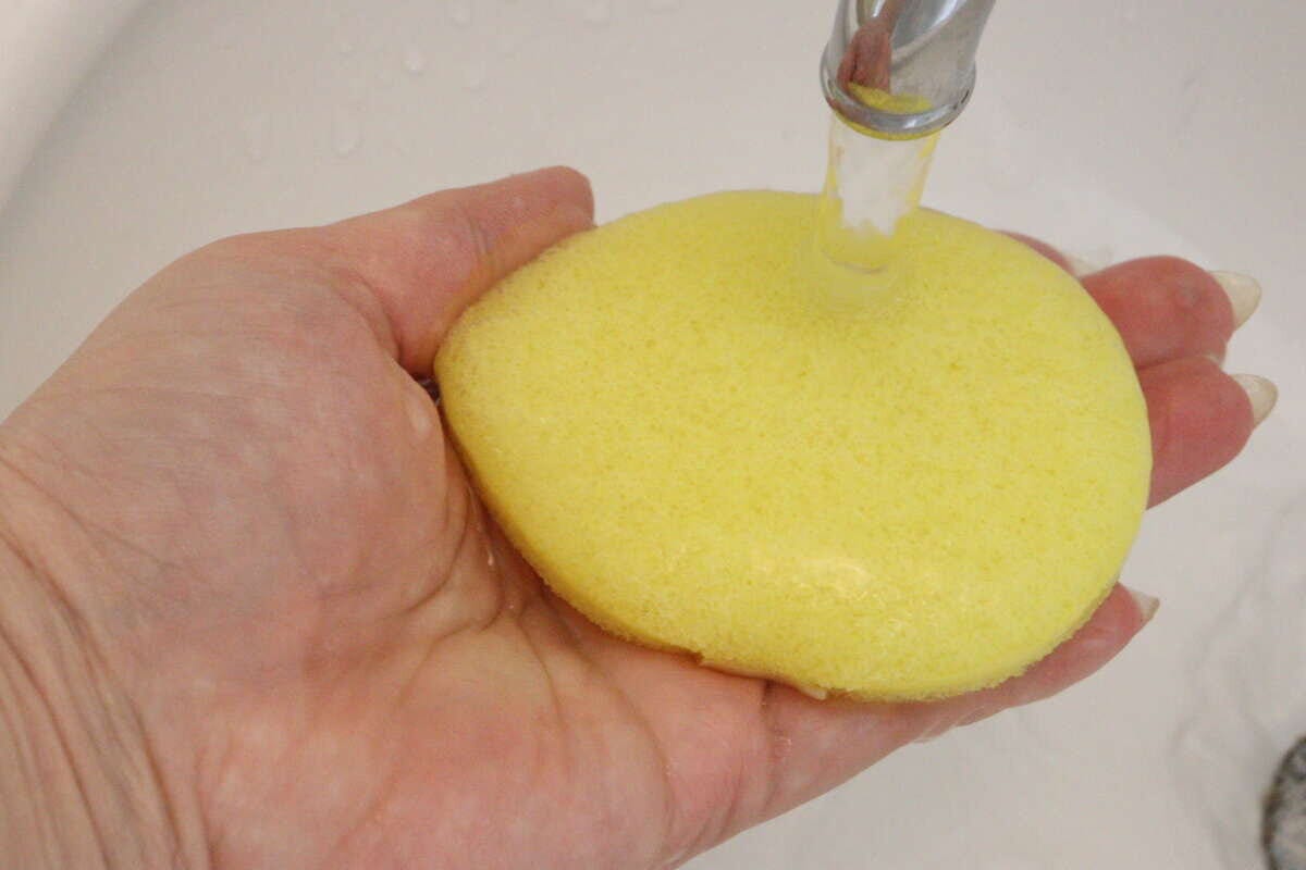 手のひらに乗せた黄色い洗顔パフに蛇口から水をかけている様子