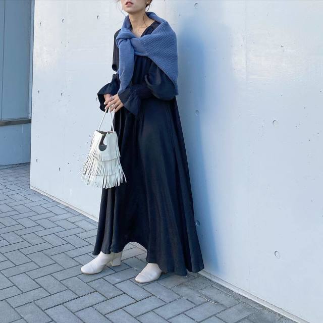 黒のワンピースにブルーのカーディガンを羽織り、白のスクエアブーツとフリンジハンドバッグをコーディネート