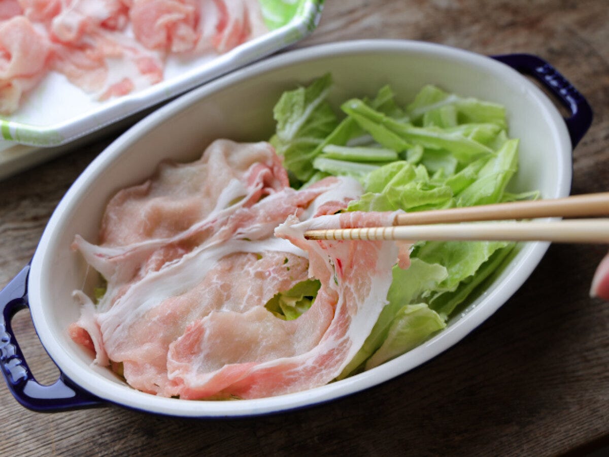 耐熱容器に敷いたキャベツの上に、しゃぶしゃぶ用の薄切り豚肉を菜箸で広げて敷き詰めている様子