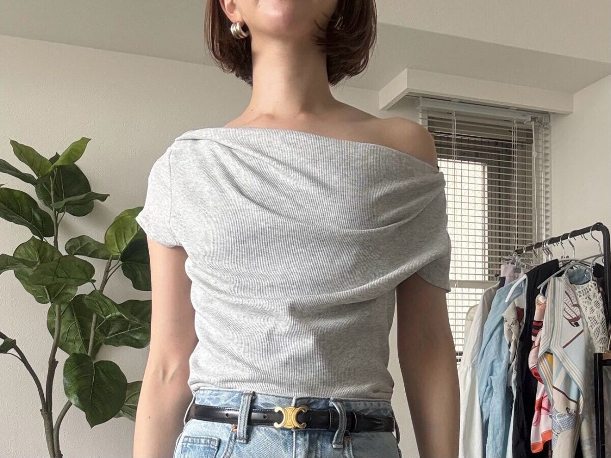女性がグレーのドレープネックTをワンショルダーで着用